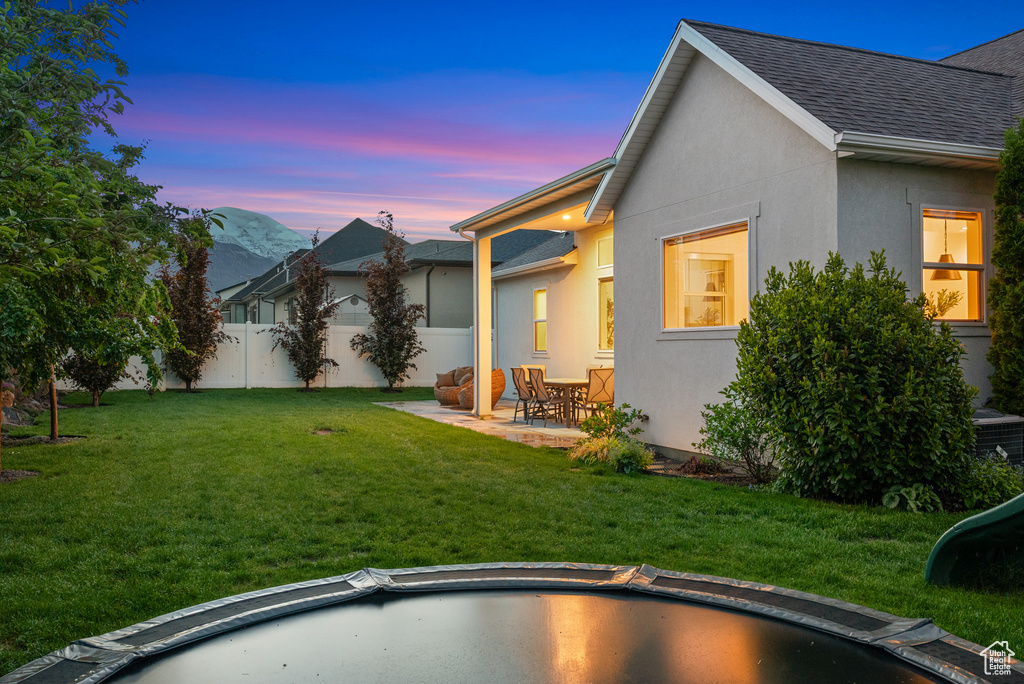 Back of house at dusk featuring stucco siding, a patio, and roof with shingles