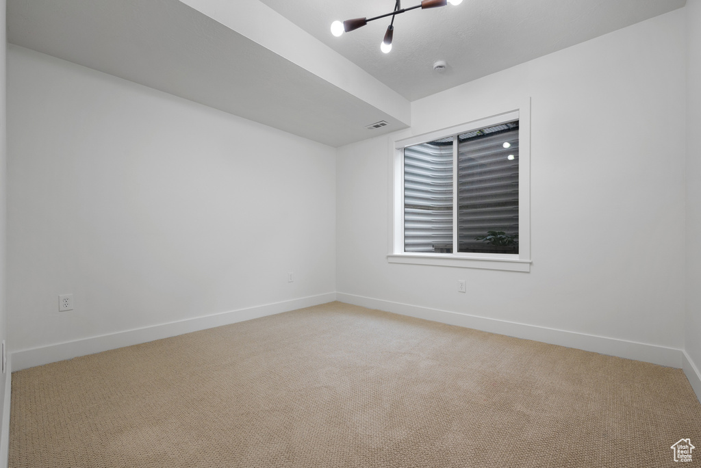 Spare room with light carpet, a chandelier, and baseboards