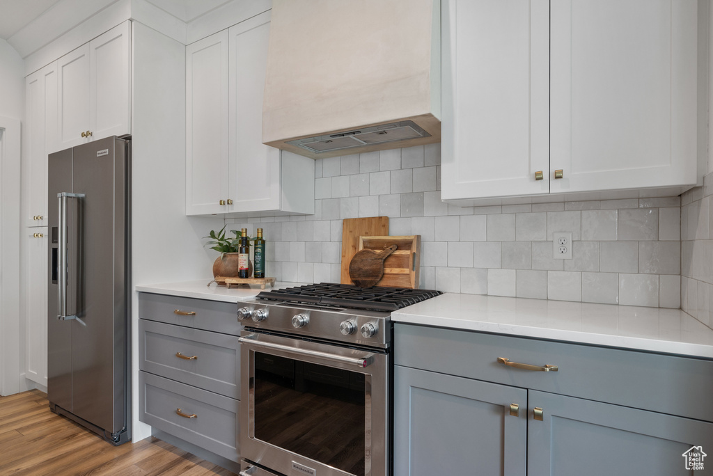 Kitchen featuring stainless steel appliances, gray cabinets, custom exhaust hood, and light countertops