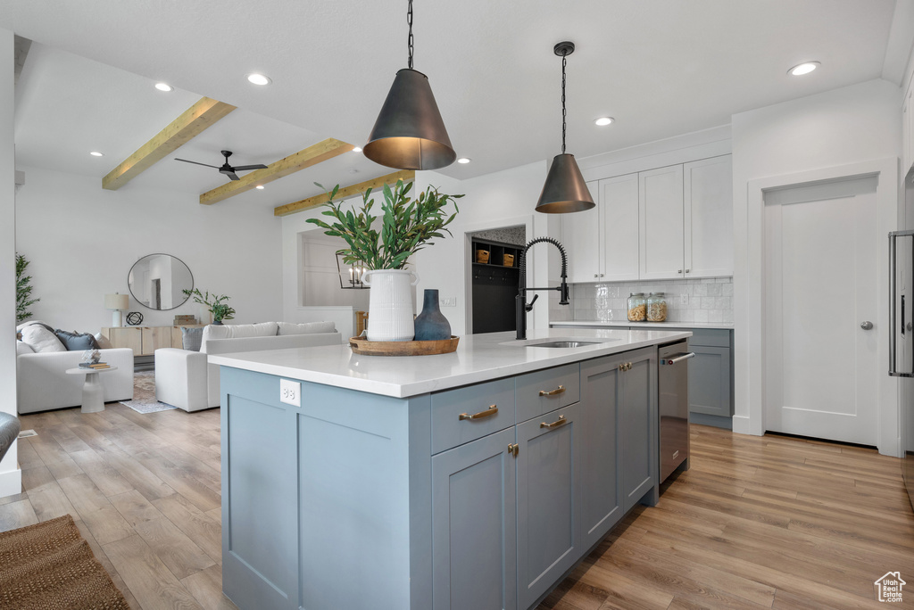 Kitchen featuring a sink, open floor plan, light countertops, light wood finished floors, and beam ceiling