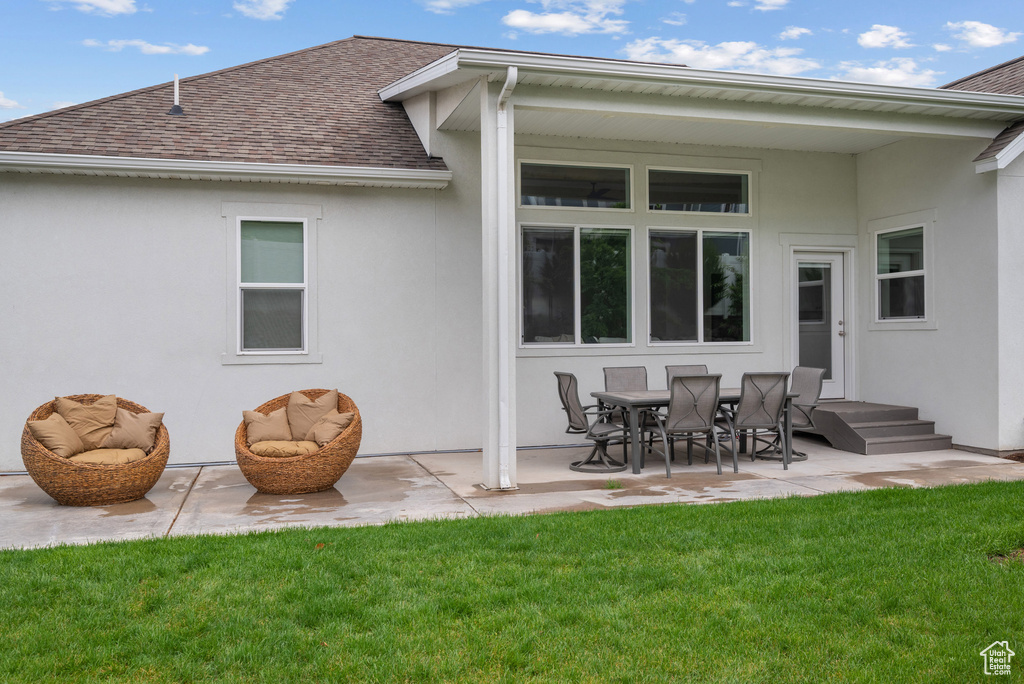 Back of house featuring roof with shingles, stucco siding, a patio, and a lawn