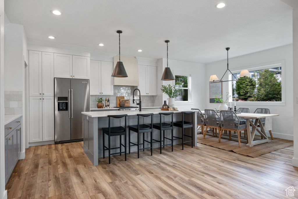 Kitchen with high quality fridge, a kitchen island with sink, tasteful backsplash, light countertops, and light wood-type flooring