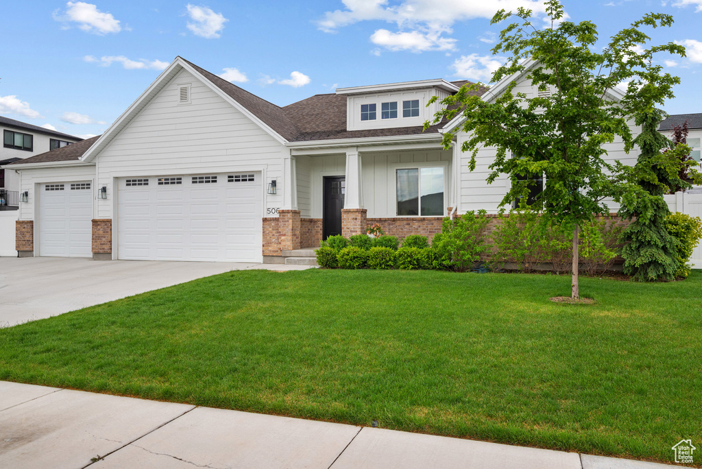 View of front of home featuring an attached garage, brick siding, a front yard, driveway, and board and batten siding