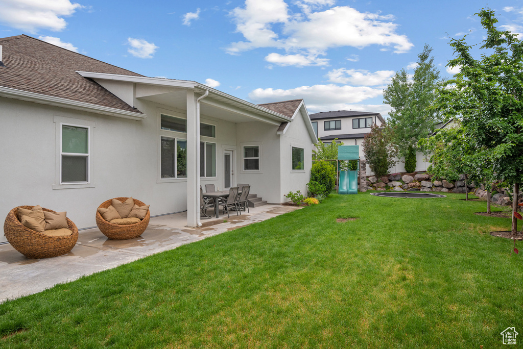 Rear view of property with a shingled roof, stucco siding, and a patio area