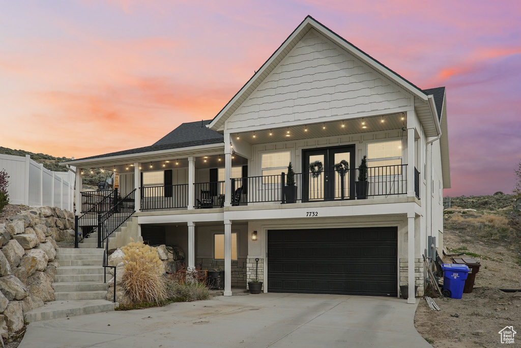 View of front of property with stairs, driveway, a balcony, an attached garage, and stone siding