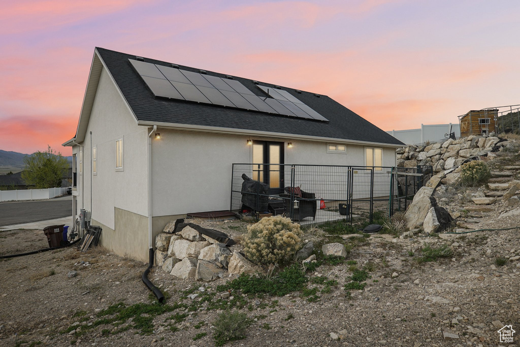 Rear view of property with solar panels, stucco siding, roof with shingles, and fence