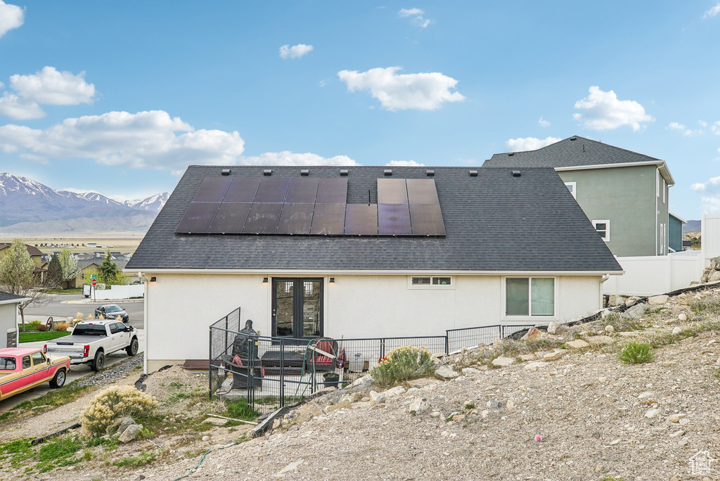 Back of property with stucco siding, solar panels, a mountain view, french doors, and fence