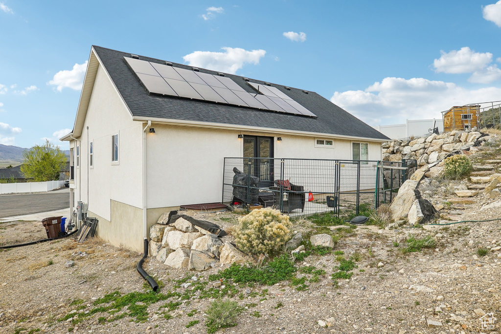 Back of property featuring roof mounted solar panels, stucco siding, a shingled roof, and fence
