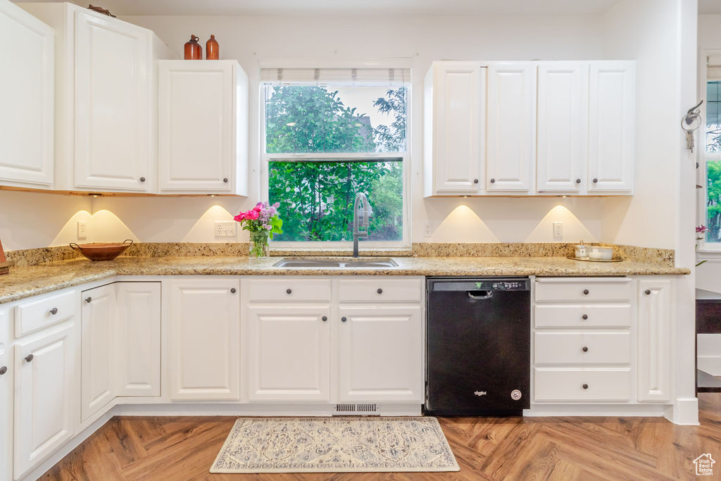 Kitchen with black dishwasher, a sink, white cabinetry, and light stone counters