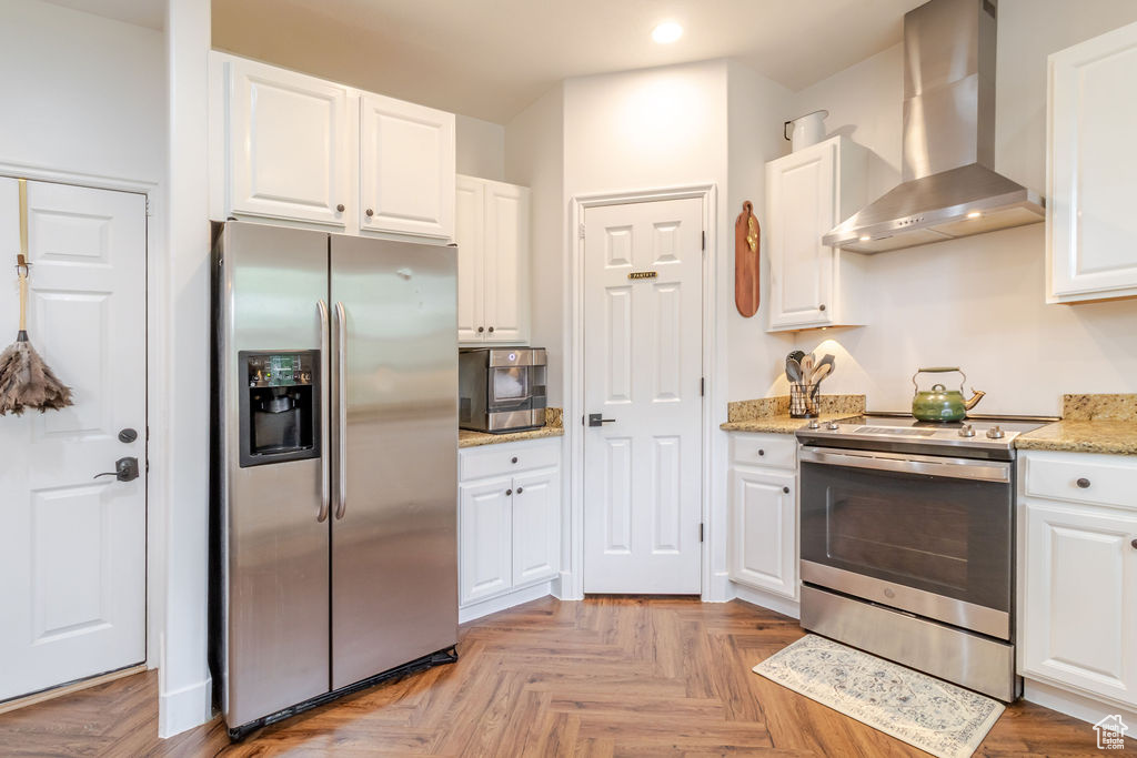 Kitchen with stainless steel appliances, wall chimney exhaust hood, recessed lighting, white cabinets, and light stone countertops