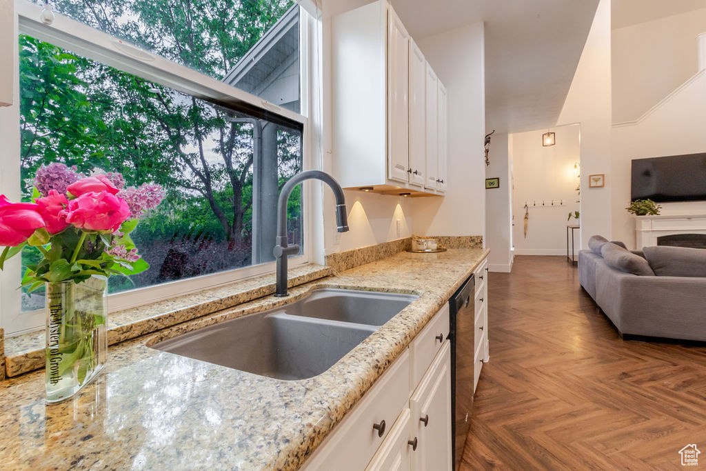 Kitchen featuring a sink, white cabinets, light stone counters, black dishwasher, and open floor plan