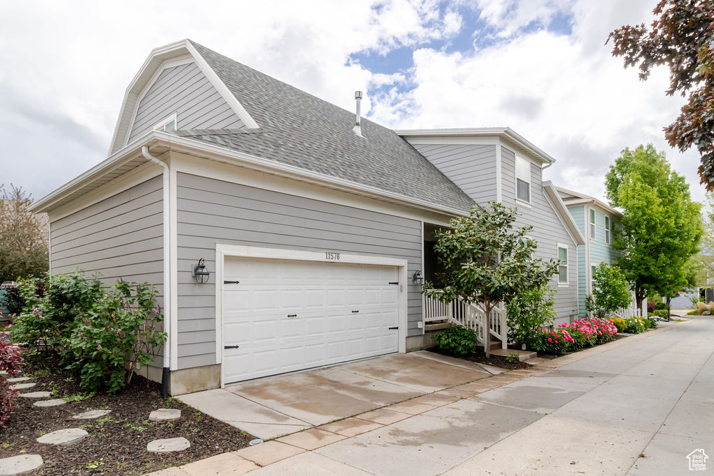 View of property exterior featuring roof with shingles, a garage, and concrete driveway