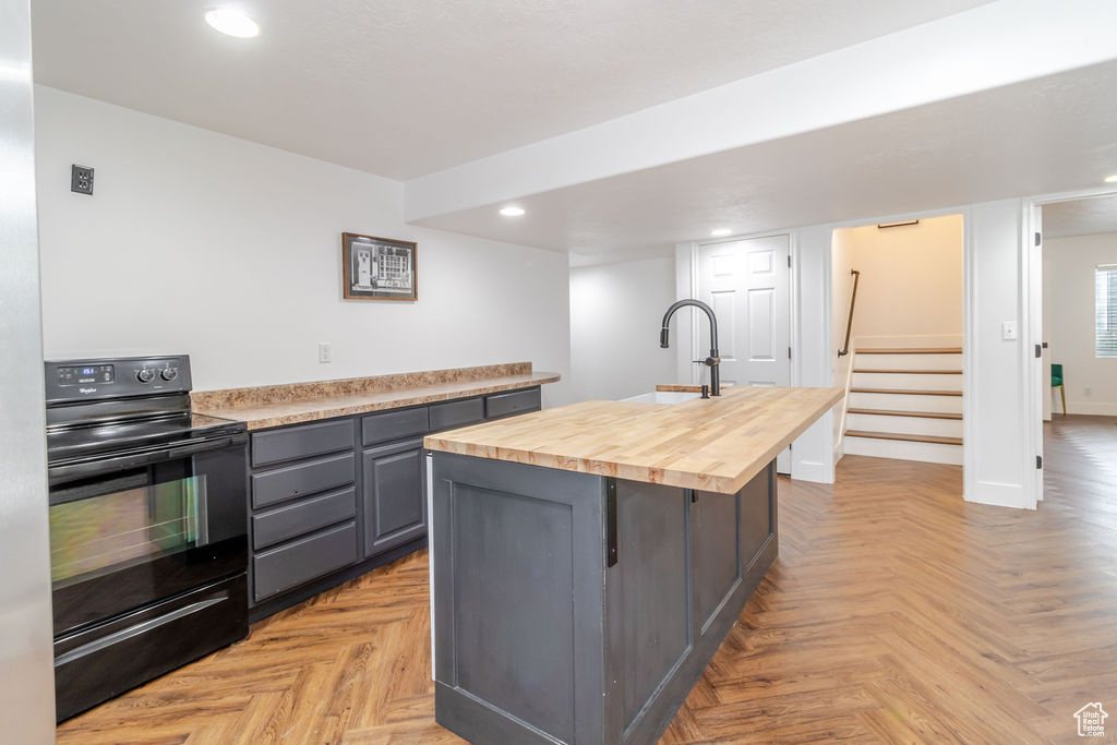 Kitchen with black / electric stove, wood counters, gray cabinets, recessed lighting, and a sink