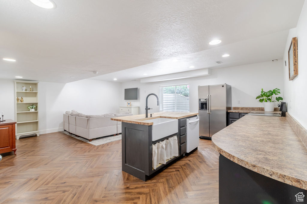 Kitchen featuring stainless steel fridge with ice dispenser, white dishwasher, a sink, a center island with sink, and recessed lighting