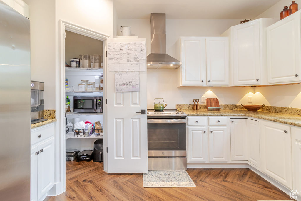 Kitchen with appliances with stainless steel finishes, wall chimney exhaust hood, and white cabinetry