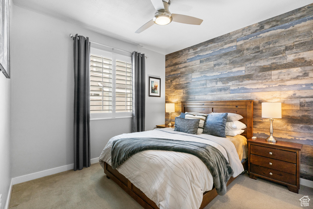 Carpeted bedroom with an accent wall, wooden walls, baseboards, and a ceiling fan