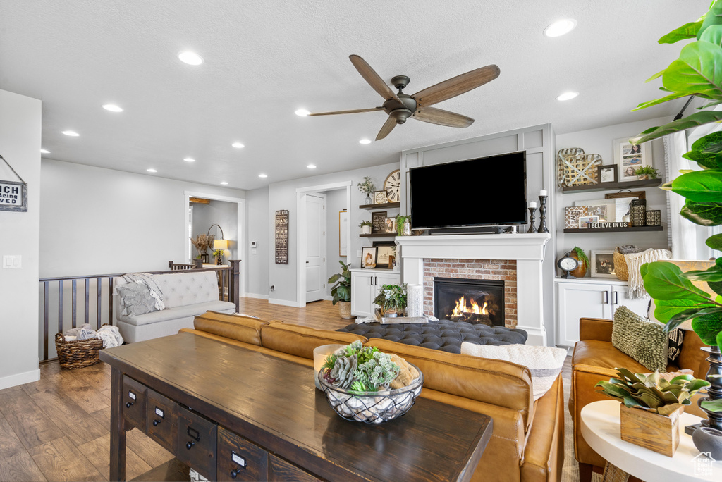 Living room featuring a ceiling fan, light wood-style floors, recessed lighting, a brick fireplace, and baseboards