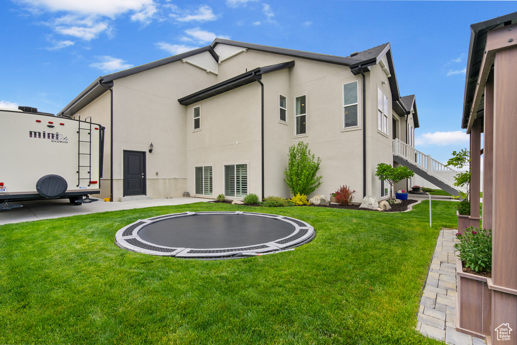 Rear view of property with a trampoline, a yard, and stucco siding
