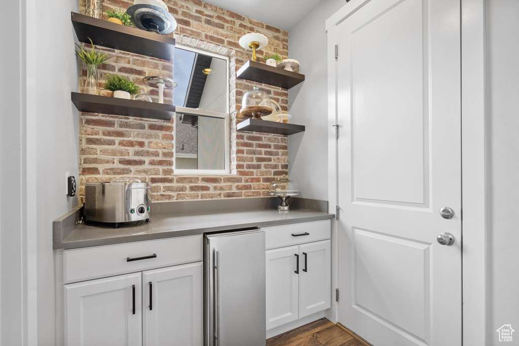 Bar area featuring high end fridge, brick wall, and wood finished floors