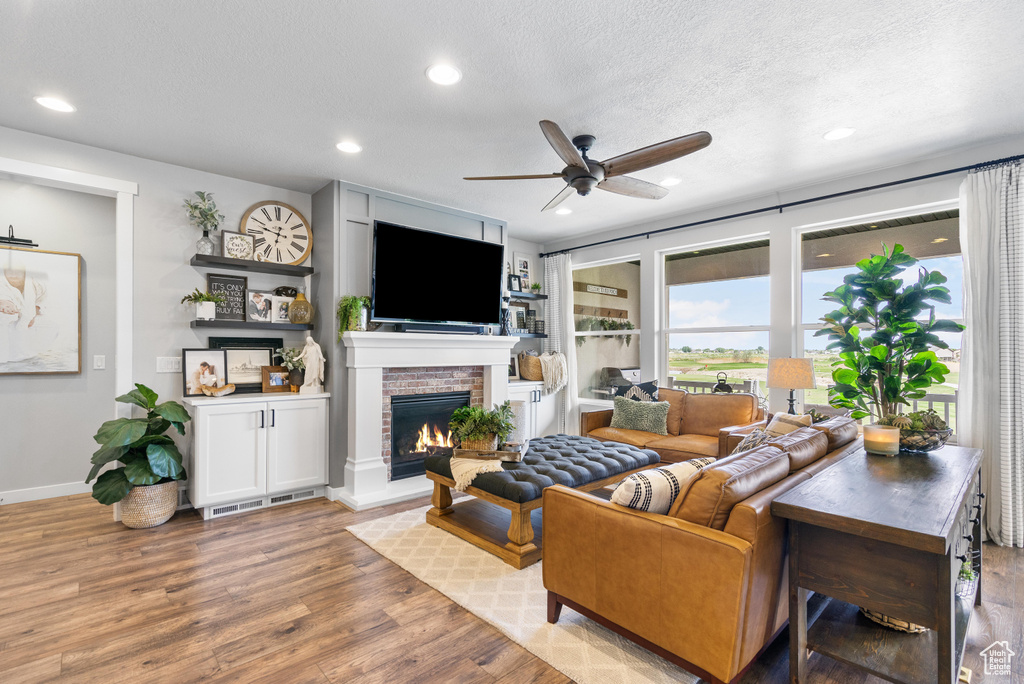 Living area with ceiling fan, wood finished floors, a fireplace, recessed lighting, and a textured ceiling
