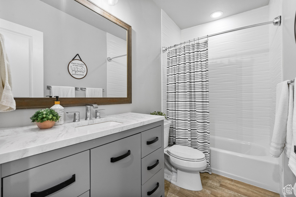 Bathroom with wood finished floors, toilet, vanity, shower / bathtub combination with curtain, and recessed lighting