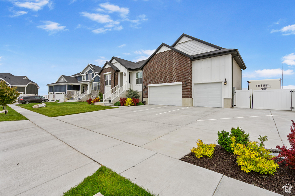 View of front of home with a gate, driveway, an attached garage, a residential view, and brick siding