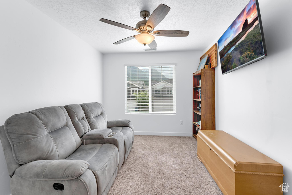 Living area featuring light colored carpet, ceiling fan, a textured ceiling, and baseboards