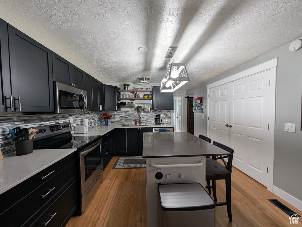 Kitchen with stainless steel appliances, open shelves, decorative backsplash, a textured ceiling, and light wood-style flooring