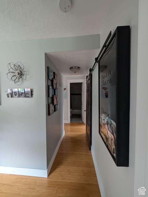Hallway with light wood-type flooring, a barn door, baseboards, and a textured ceiling