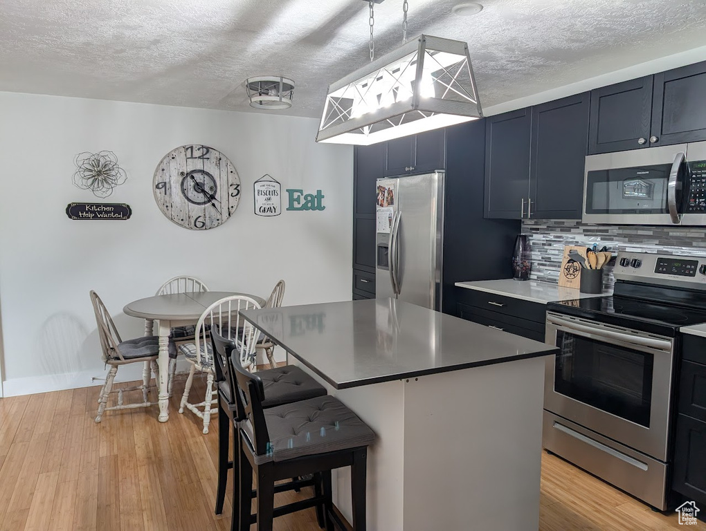 Kitchen with stainless steel appliances, a breakfast bar, backsplash, a textured ceiling, and light wood-type flooring