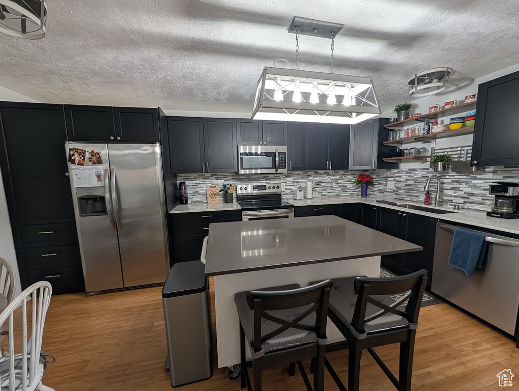 Kitchen with stainless steel appliances, a sink, a textured ceiling, open shelves, and a center island