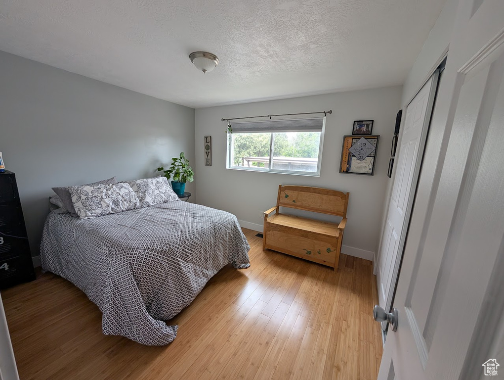 Bedroom with light wood finished floors, baseboards, and a textured ceiling