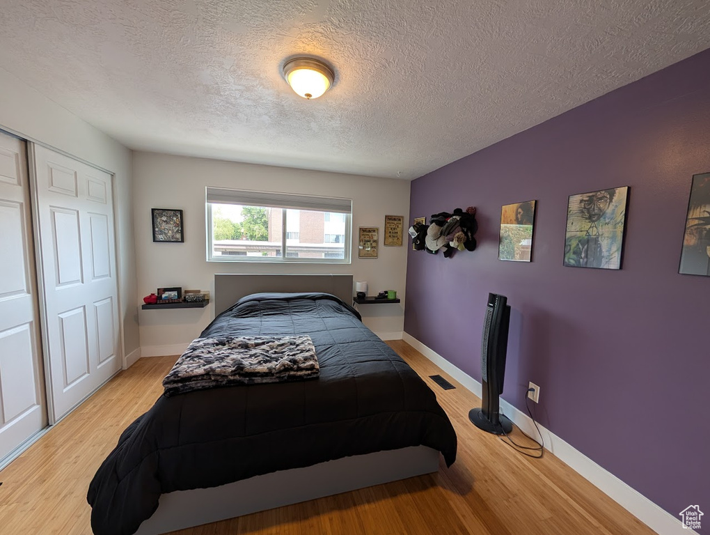 Bedroom with light wood finished floors, a textured ceiling, baseboards, and a closet