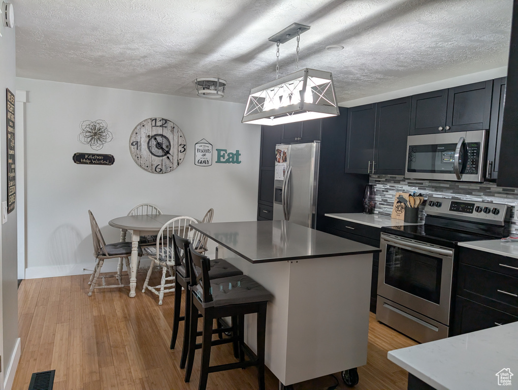 Kitchen with appliances with stainless steel finishes, a textured ceiling, a kitchen bar, backsplash, and light countertops