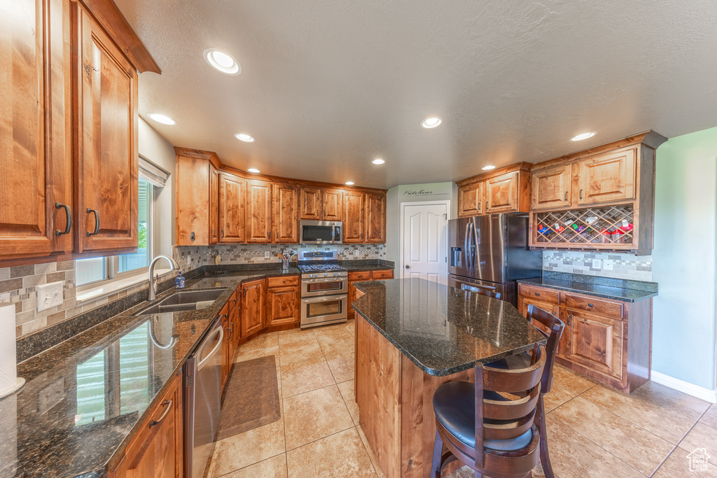 Kitchen with stainless steel appliances, a sink, backsplash, a center island, and light tile patterned floors