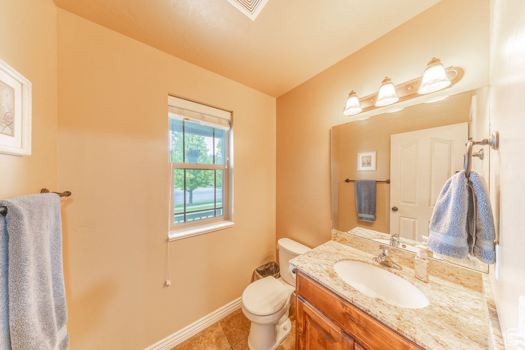 Half bathroom with toilet, tile patterned floors, vanity, and baseboards