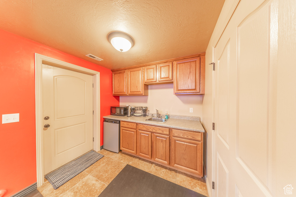 Kitchen featuring stainless steel dishwasher, a sink, light countertops, black microwave, and a textured ceiling