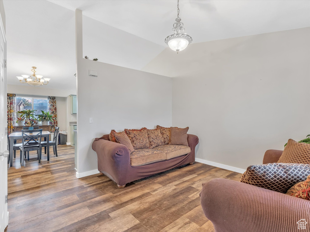 Living area featuring a chandelier, wood finished floors, baseboards, and lofted ceiling