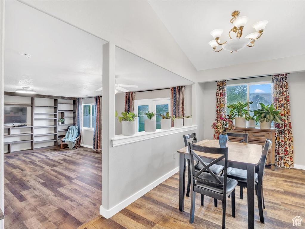 Dining space featuring plenty of natural light, baseboards, a chandelier, wood finished floors, and lofted ceiling