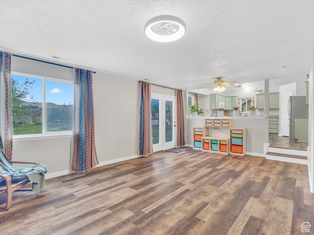 Unfurnished living room with a textured ceiling, wood finished floors, baseboards, and a ceiling fan