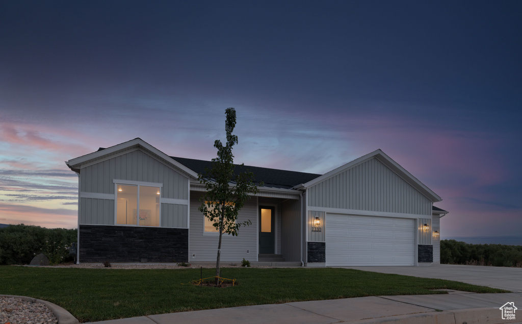 View of front of house with stone siding, board and batten siding, a garage, driveway, and a lawn