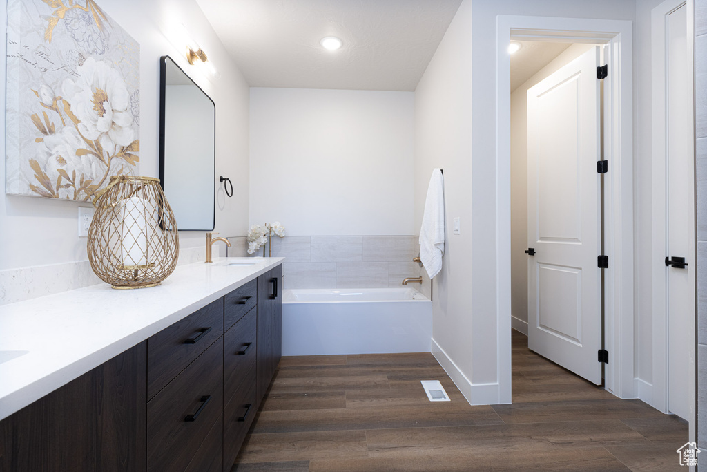 Full bathroom featuring wood finished floors, double vanity, a bath, recessed lighting, and baseboards