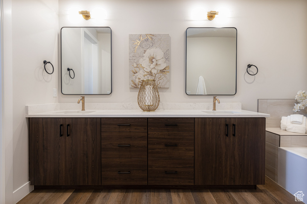 Full bath with double vanity, wood finished floors, and a bathtub