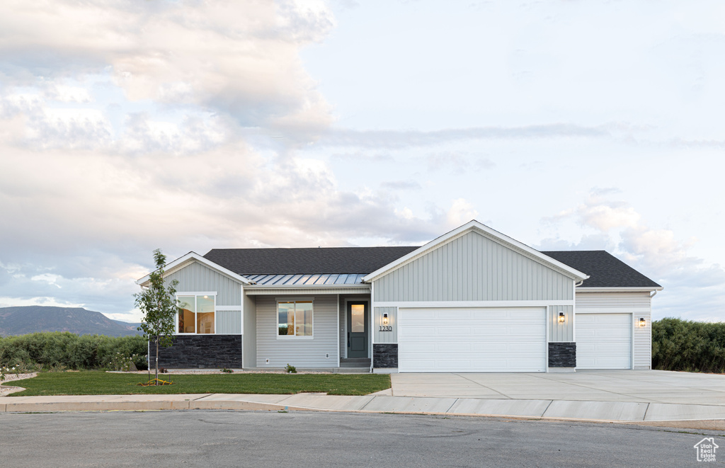 View of front facade with an attached garage, board and batten siding, concrete driveway, a standing seam roof, and stone siding