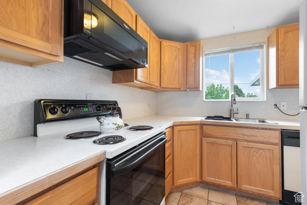 Kitchen with electric range, black microwave, a sink, and light countertops