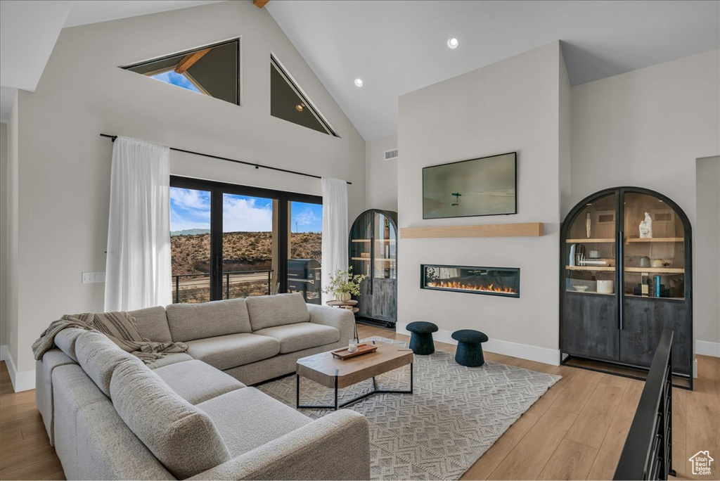 Living room featuring high vaulted ceiling, wood finished floors, baseboards, a glass covered fireplace, and recessed lighting