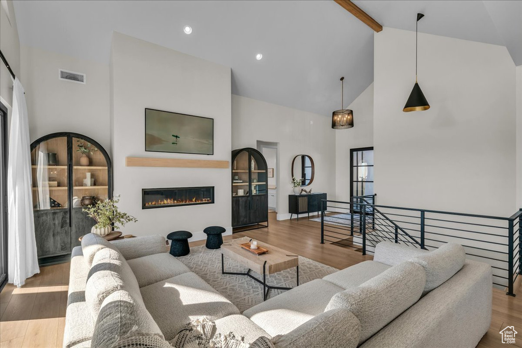Living room with high vaulted ceiling, beamed ceiling, wood finished floors, and a glass covered fireplace