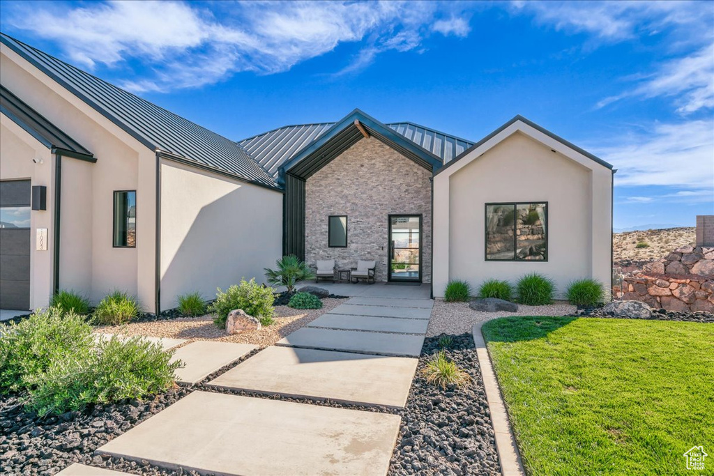 View of front of house with a standing seam roof, metal roof, a front yard, stucco siding, and stone siding