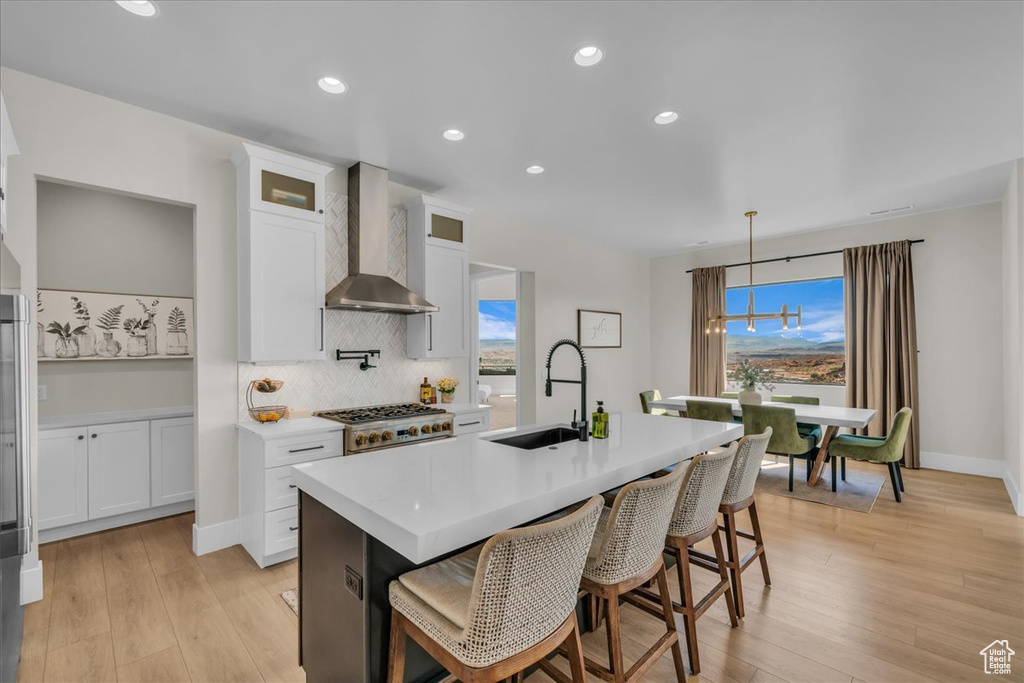 Kitchen featuring wall chimney exhaust hood, a sink, tasteful backsplash, a kitchen island with sink, and light countertops