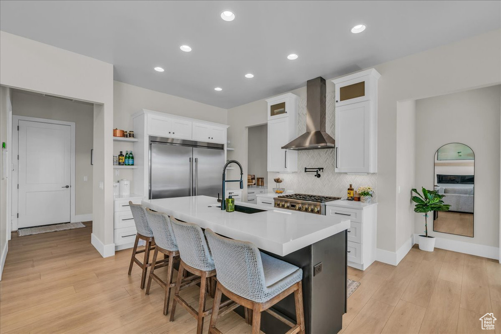 Kitchen with wall chimney exhaust hood, appliances with stainless steel finishes, a sink, tasteful backsplash, and light wood finished floors